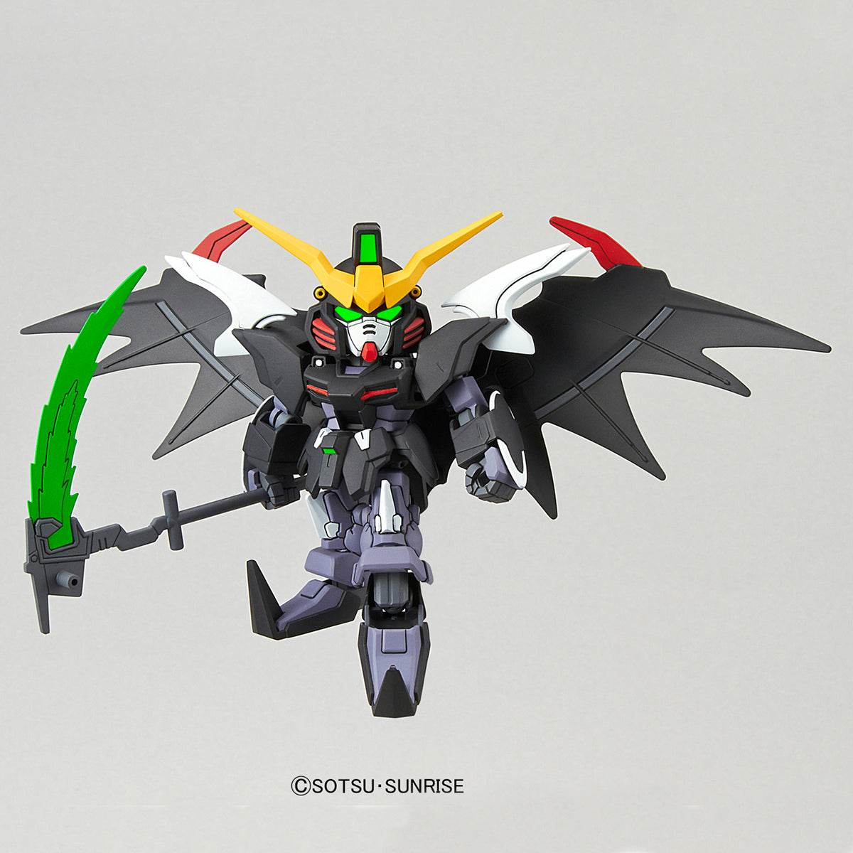 A small Gundam-style robot figure with black wings, a yellow and white head, green eyes, and a green blade, shown against a plain light gray background. A small 'SOTSU SUNRISE' copyright mark appears below the figure.