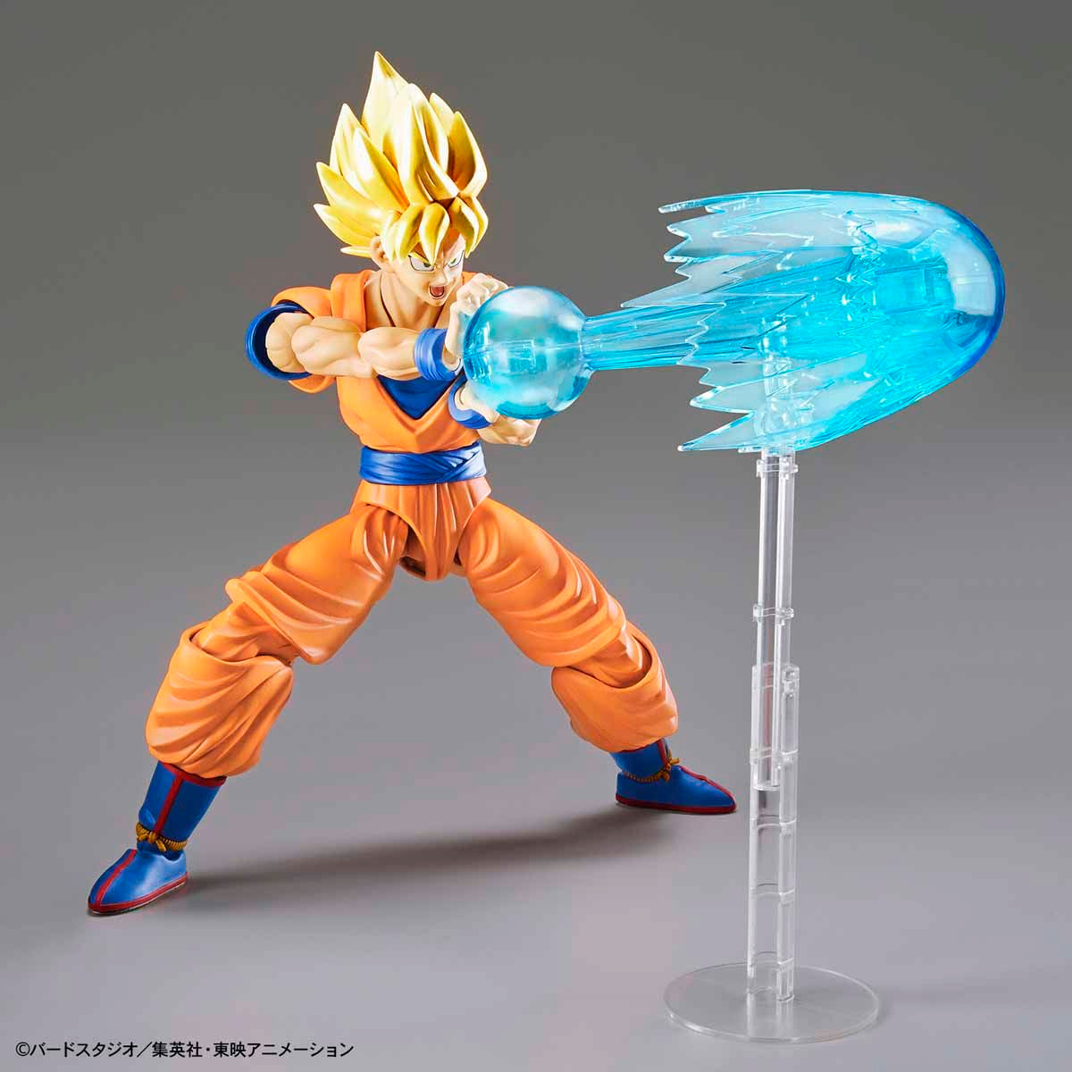 Action figure of a character in an orange and blue outfit with a blue energy blast on a gray background