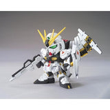 A small white and black Gundam action figure holding a rifle in one hand and a large shield-like weapon in the other, photographed against a plain gray studio background.