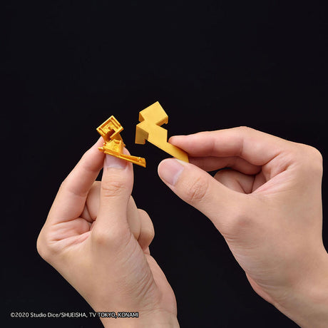 Two hands holding small golden plastic dice against a solid black background. A copyright watermark for Studio Dice/Shueisha TV Tokyo MX Kanjiama is visible in the bottom-left corner.