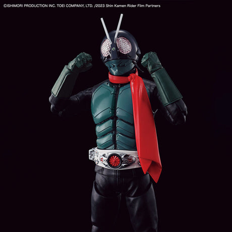 Kamen Rider Shin Kamen Rider action figure posed with arms raised, wearing a dark green and black bodysuit with a bright red cape and silver belt, set against a solid black background.
