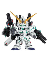 A small white mecha toy figure with gold horn-like antennas, green facial details, black weapon attachments, and blue feet, shown against a plain white background.
